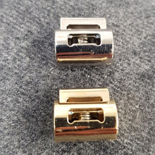 Lataa kuva Galleria-katseluun, Erittäin kevyt ja tyylikäs nyörinkiristin max. 8 mm nauhalle. Sopii mainiosti takkien ja huppareiden nauhan kiristimeksi. Materiaali on metalliväreiksi galvanoitua muovia. Leveys 16 mm, korkeus 14mm. Värit hopea ja kulta.
